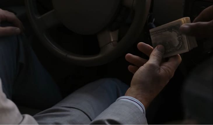 Man passing large fold of cash inside car