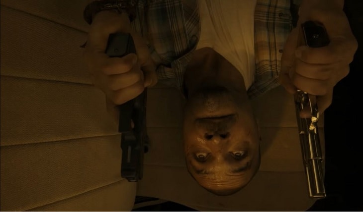 Nacho holding twin pistols lying down inside a truck