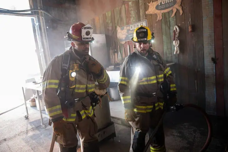 Fire Country S4E6: Two firefighters navigate a smoky kitchen with hose and flashlights